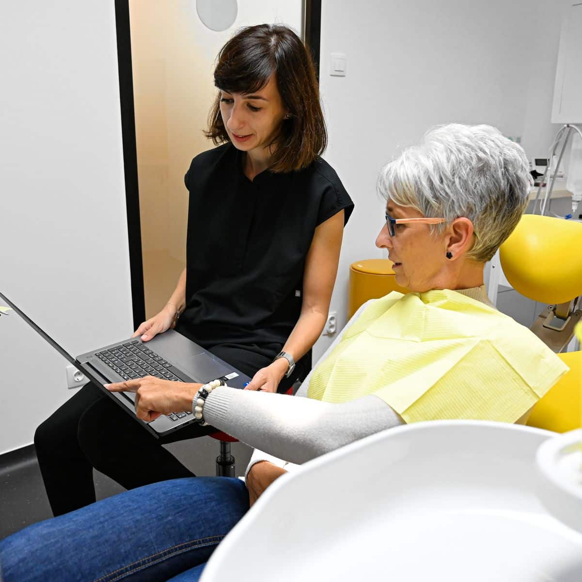 Fogpótlás előtt fogorvos kezében egy laptoppal és páciens aki rámutat