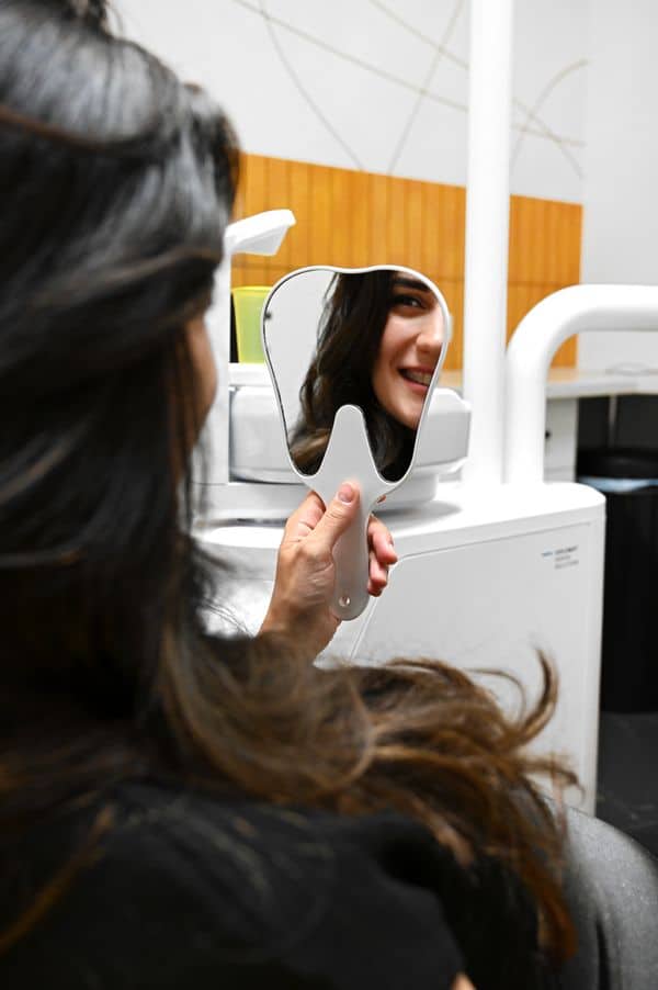 Fogszabályozás után fiatal nő kis tükörben nézi az eredményt